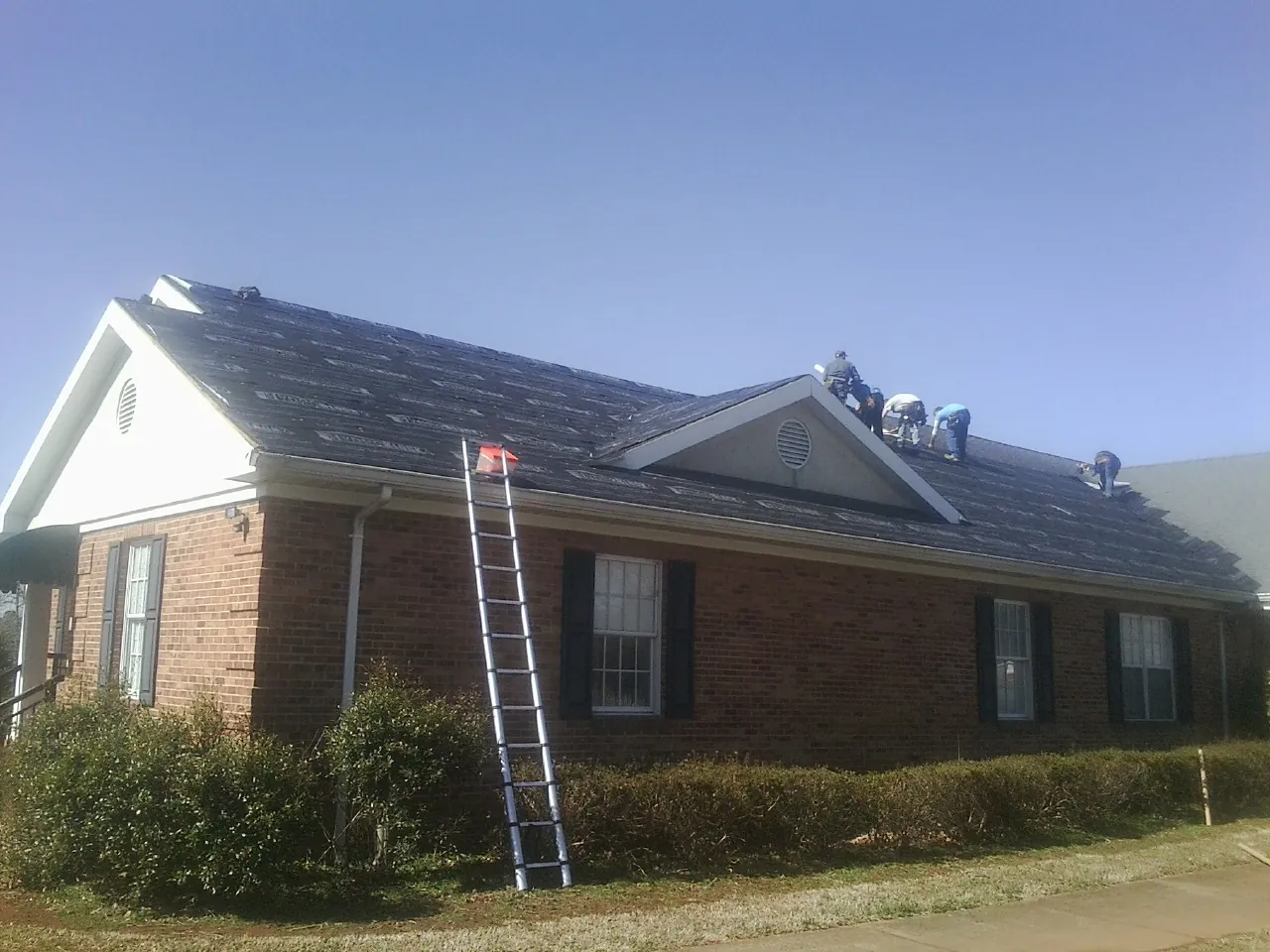 Crew tearing shingles off a brick ranch roof with a ladder set — Emergency Roof Repair work by our crew in Aroma Park