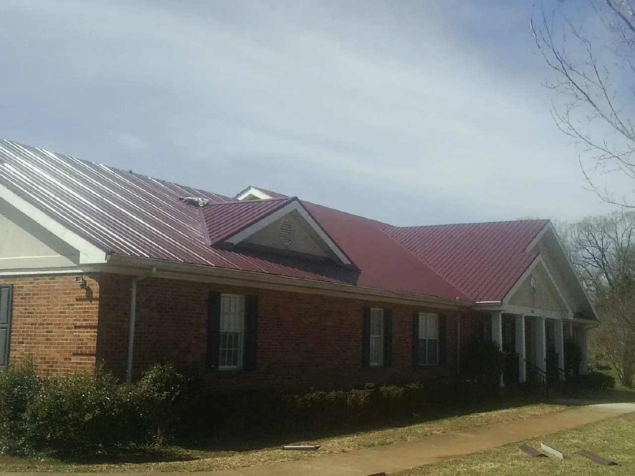 Red metal roof with gabled entries on a long brick building, from a Hail Damage Roof Repair job in Aroma Park