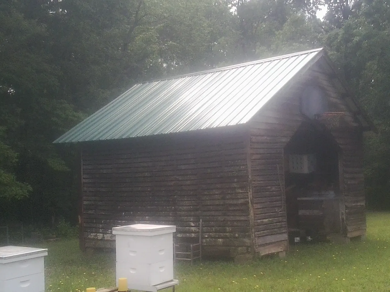 Green metal roof on a weathered barn beside stacked beehives in Aroma Park