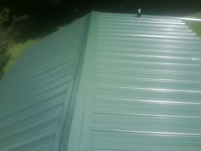 New green metal panels meeting at the ridge of a roof — Flat Roof Repair work by our crew in Aroma Park