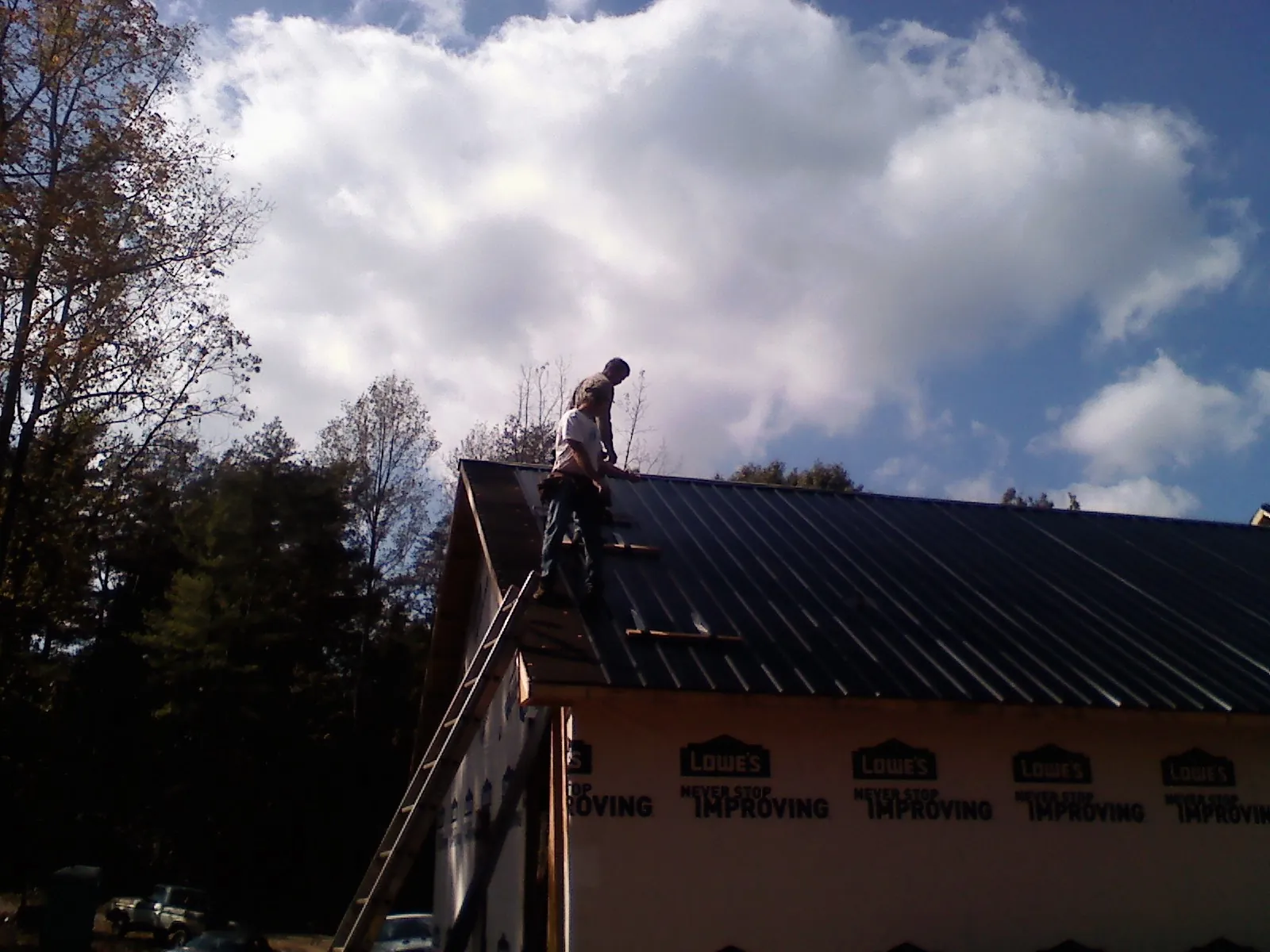 Roofer fastening dark metal panels high against a cloudy sky, from a Roof Inspection job in Aroma Park