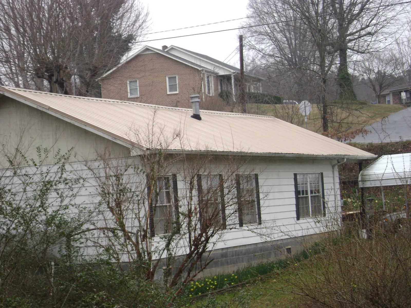 Tan metal roof on a white sided house set into a hillside — Commercial Roofing by Roofing Brothers in Aroma Park